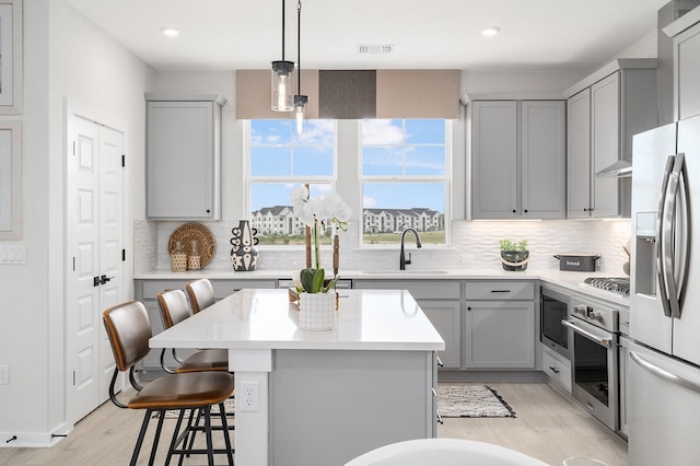 kitchen with sink, gray cabinetry, decorative light fixtures, a kitchen breakfast bar, and stainless steel appliances