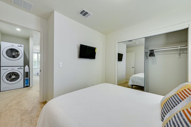 carpeted bedroom with stacked washer and dryer, visible vents, and a closet