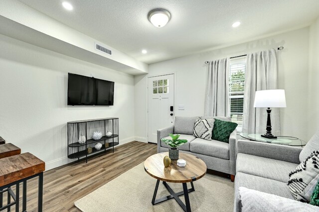 living room with recessed lighting, visible vents, baseboards, and wood finished floors