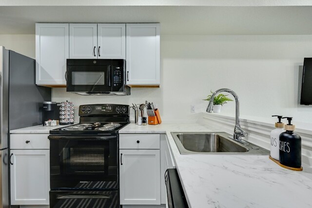 kitchen with light stone counters, white cabinetry, black appliances, and a sink