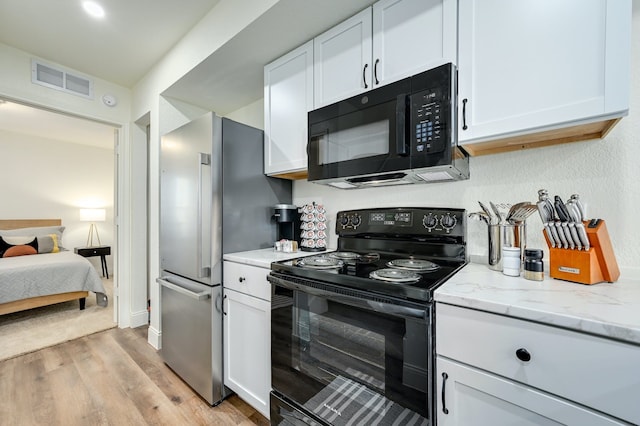 kitchen with white cabinetry, light stone counters, light hardwood / wood-style flooring, and black appliances