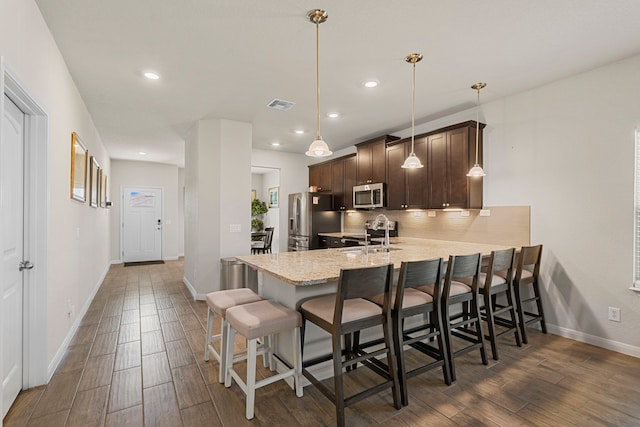 kitchen with appliances with stainless steel finishes, a kitchen breakfast bar, hanging light fixtures, kitchen peninsula, and dark brown cabinets