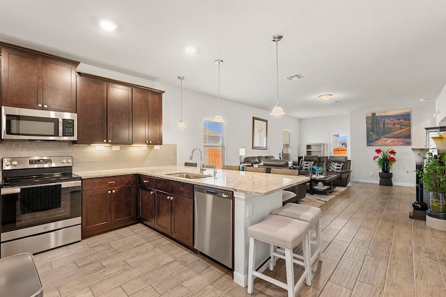 kitchen with appliances with stainless steel finishes, decorative light fixtures, sink, a kitchen breakfast bar, and kitchen peninsula