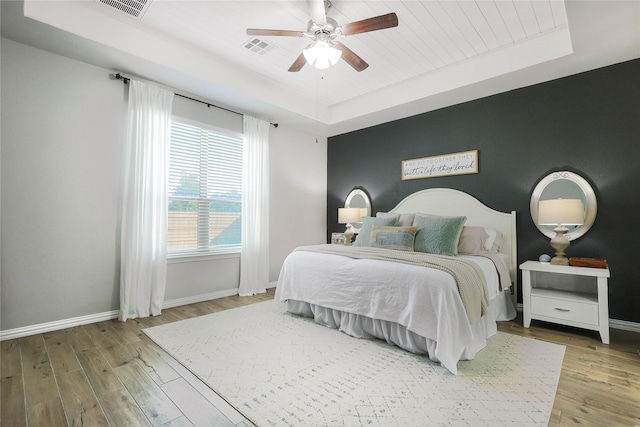 bedroom with wood-type flooring, ceiling fan, and a tray ceiling