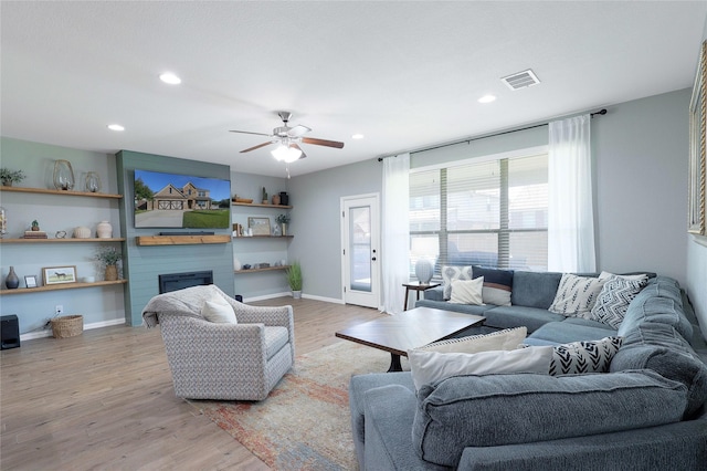 living room with light hardwood / wood-style floors, a large fireplace, and ceiling fan