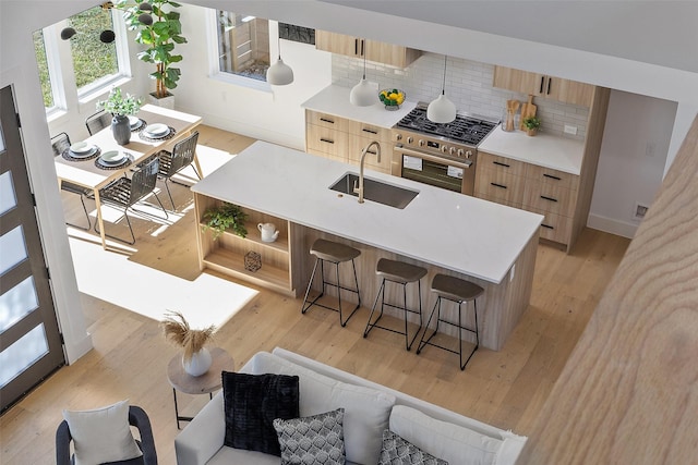 kitchen with sink, a breakfast bar area, an island with sink, high end stainless steel range oven, and decorative backsplash