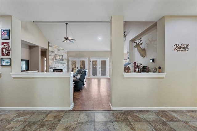 kitchen featuring lofted ceiling, ceiling fan, french doors, a stone fireplace, and kitchen peninsula