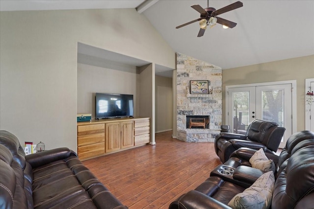 living room featuring a stone fireplace, beamed ceiling, wood-type flooring, ceiling fan, and french doors