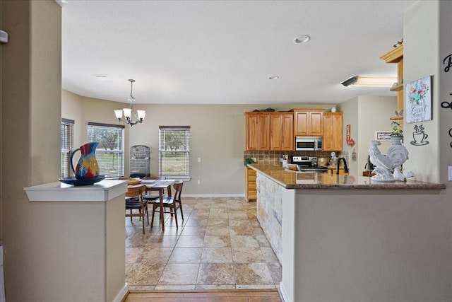 kitchen with stone countertops, hanging light fixtures, kitchen peninsula, stainless steel appliances, and decorative backsplash