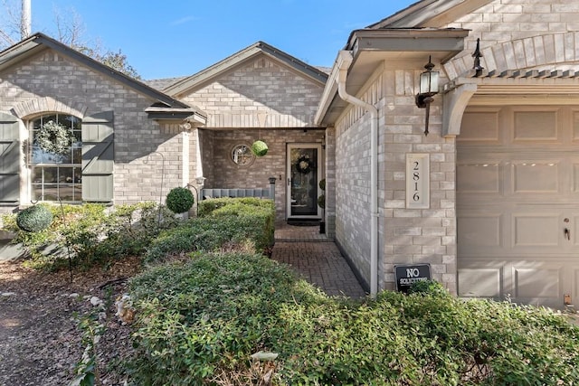 doorway to property featuring a garage and brick siding