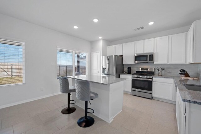 305 Ravens Crest Dr, Hutto, TX 78634 - kitchen featuring appliances with stainless steel finishes, decorative backsplash, light stone countertops, a kitchen island, and a kitchen breakfast bar