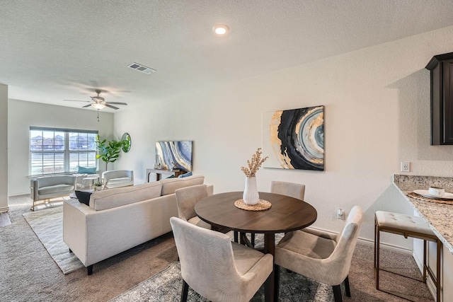 dining space with ceiling fan, light colored carpet, and a textured ceiling