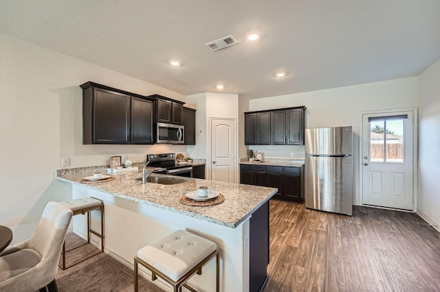 kitchen with a kitchen bar, light stone counters, appliances with stainless steel finishes, dark hardwood / wood-style floors, and kitchen peninsula