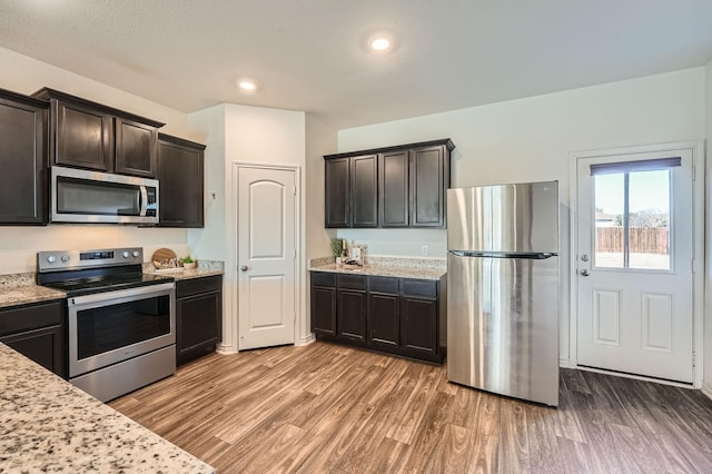 kitchen featuring dark brown cabinetry, appliances with stainless steel finishes, hardwood / wood-style floors, and light stone counters