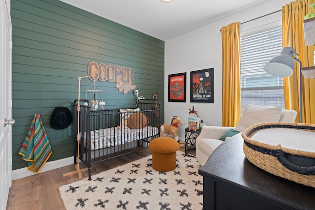 bedroom with a nursery area, dark hardwood / wood-style floors, and wood walls