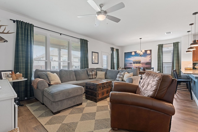 living room with ceiling fan with notable chandelier, plenty of natural light, and light hardwood / wood-style floors