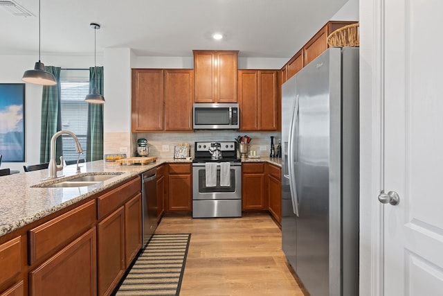 kitchen with pendant lighting, tasteful backsplash, sink, stainless steel appliances, and light stone countertops