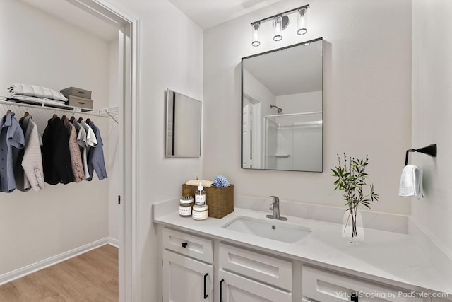 full bath featuring baseboards, a shower, wood finished floors, a spacious closet, and vanity