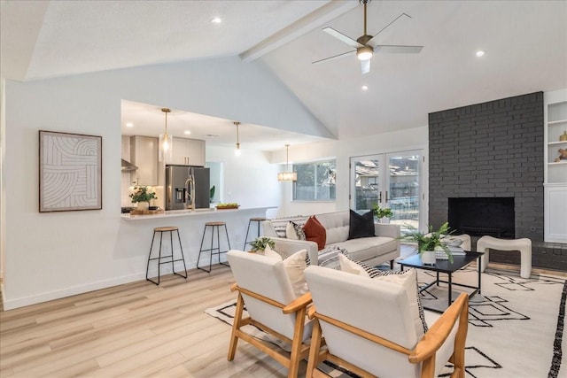 living room featuring high vaulted ceiling, light hardwood / wood-style flooring, beamed ceiling, ceiling fan, and a fireplace