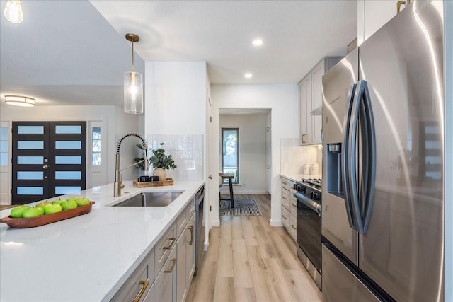 kitchen featuring pendant lighting, light wood-style flooring, a sink, backsplash, and appliances with stainless steel finishes