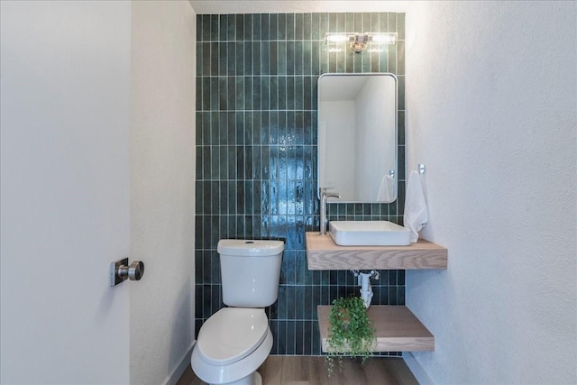 half bathroom with tile walls, toilet, wood finished floors, and a sink