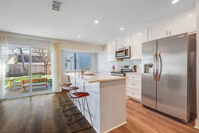 kitchen with stainless steel appliances, an island with sink, and white cabinets