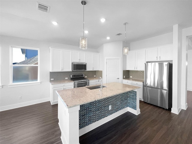 kitchen with pendant lighting, white cabinetry, stainless steel appliances, light stone countertops, and a center island with sink