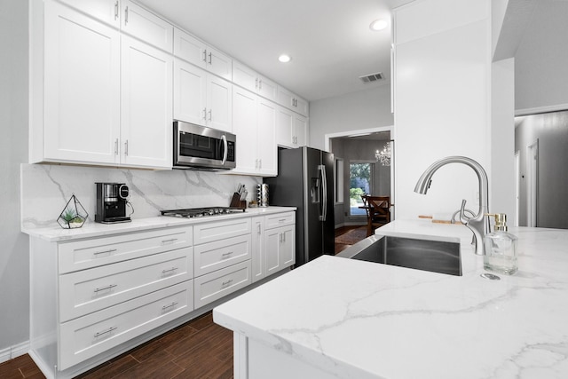 kitchen with stainless steel appliances, white cabinetry, sink, and light stone counters