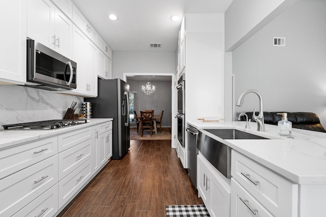 kitchen featuring appliances with stainless steel finishes, white cabinetry, sink, backsplash, and light stone counters