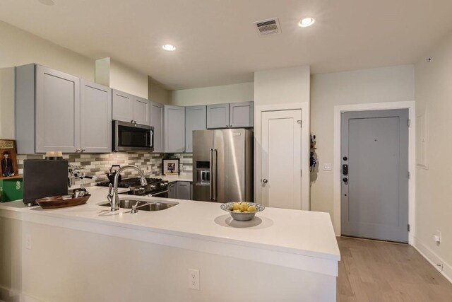 kitchen featuring tasteful backsplash, sink, premium appliances, kitchen peninsula, and light hardwood / wood-style flooring