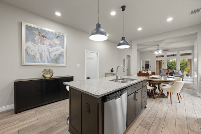 kitchen featuring sink, hanging light fixtures, stainless steel dishwasher, light stone countertops, and a kitchen island with sink