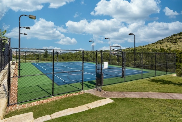 view of tennis court with a yard and basketball hoop