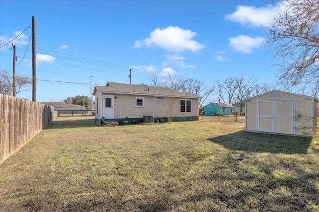 rear view of property featuring a storage unit, an outbuilding, central AC, a fenced backyard, and a yard