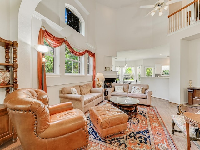 living room with crown molding, ceiling fan, light wood-type flooring, and a high ceiling