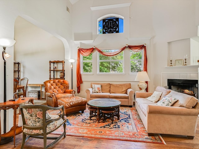 living room with a tiled fireplace, hardwood / wood-style floors, and a high ceiling