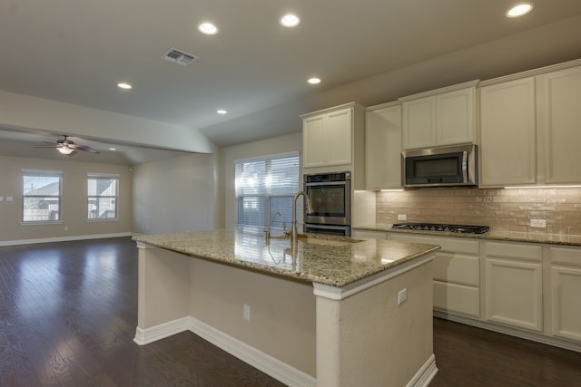 kitchen with white cabinetry, stainless steel appliances, light stone countertops, a center island with sink, and vaulted ceiling