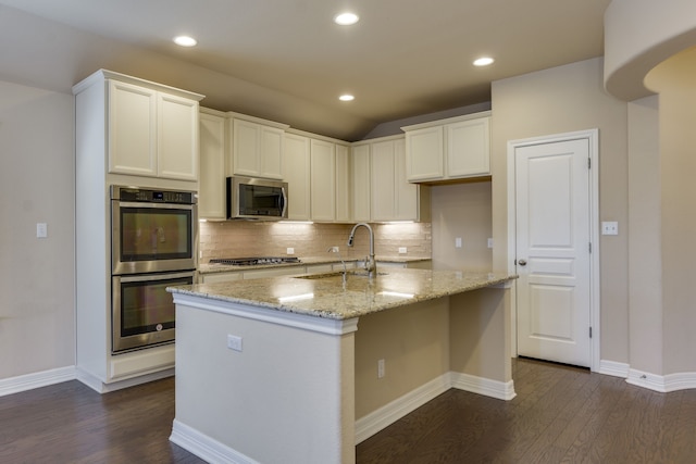 kitchen featuring appliances with stainless steel finishes, sink, white cabinets, a kitchen island with sink, and light stone counters