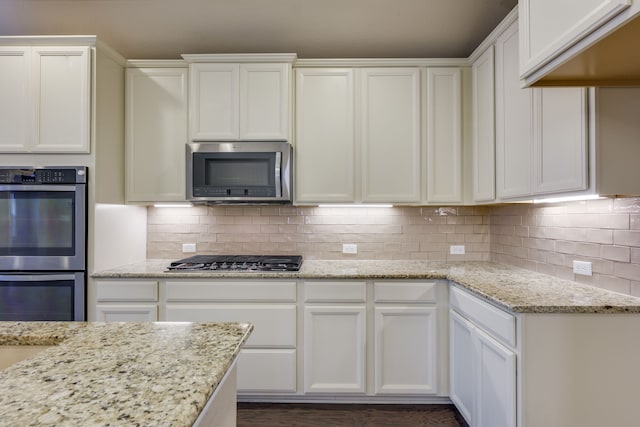 kitchen featuring white cabinetry, appliances with stainless steel finishes, light stone countertops, and decorative backsplash