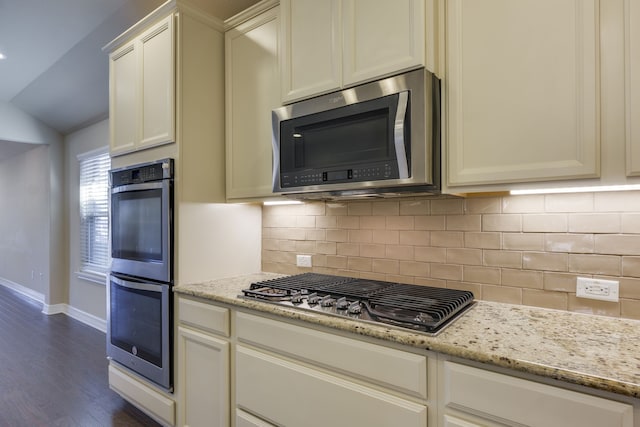 kitchen with dark hardwood / wood-style flooring, appliances with stainless steel finishes, lofted ceiling, and light stone counters