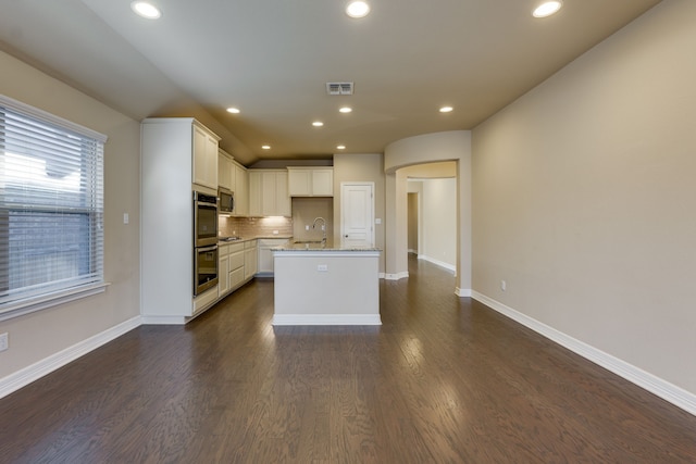 kitchen featuring dark hardwood / wood-style floors, white cabinetry, backsplash, light stone counters, and a center island with sink