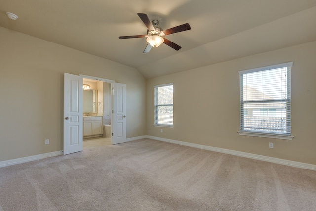 unfurnished bedroom with multiple windows, vaulted ceiling, connected bathroom, and ceiling fan