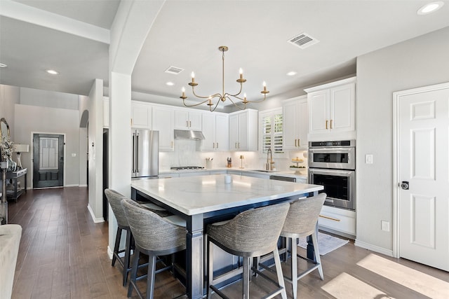 kitchen featuring white cabinetry, sink, a kitchen bar, hanging light fixtures, and a center island