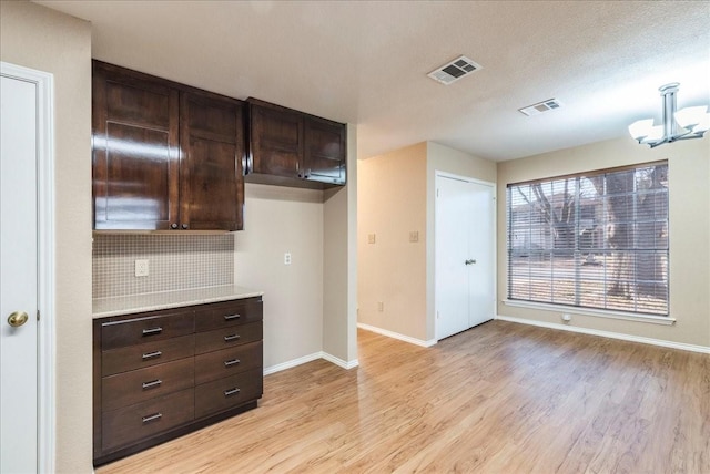 kitchen with dark brown cabinets, light hardwood / wood-style floors, hanging light fixtures, and backsplash