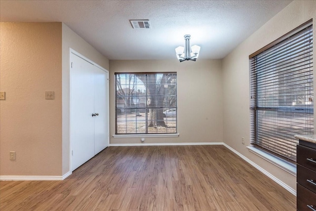 unfurnished dining area featuring an inviting chandelier, light hardwood / wood-style floors, and a textured ceiling