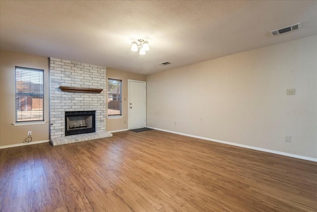 unfurnished living room featuring a brick fireplace, hardwood / wood-style flooring, and a textured ceiling