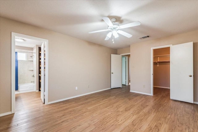 unfurnished bedroom with ceiling fan, a walk in closet, a closet, and light hardwood / wood-style flooring