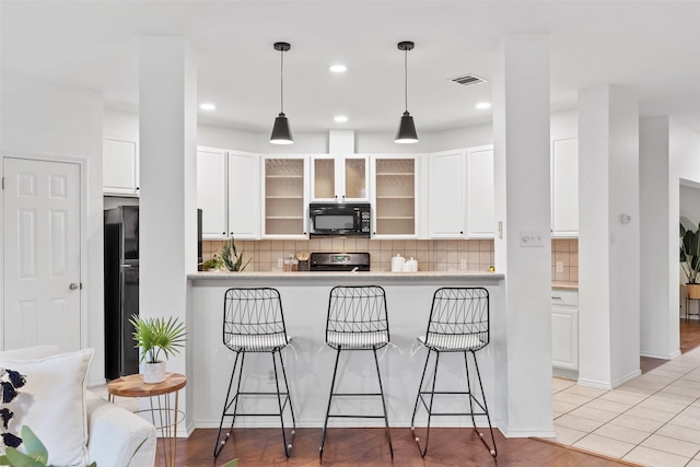 kitchen featuring white cabinetry, a kitchen breakfast bar, and black appliances