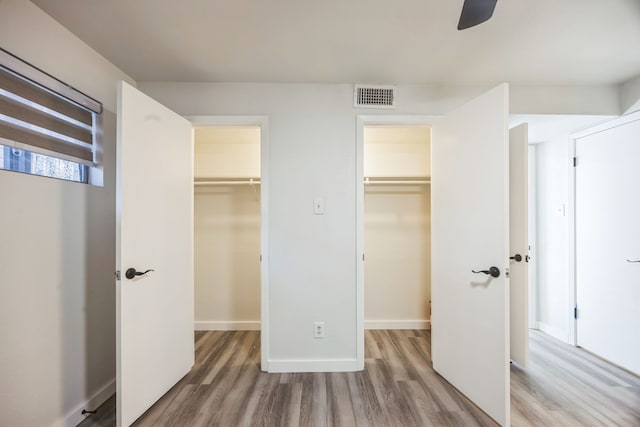 unfurnished bedroom featuring ceiling fan, a walk in closet, wood-type flooring, and a closet