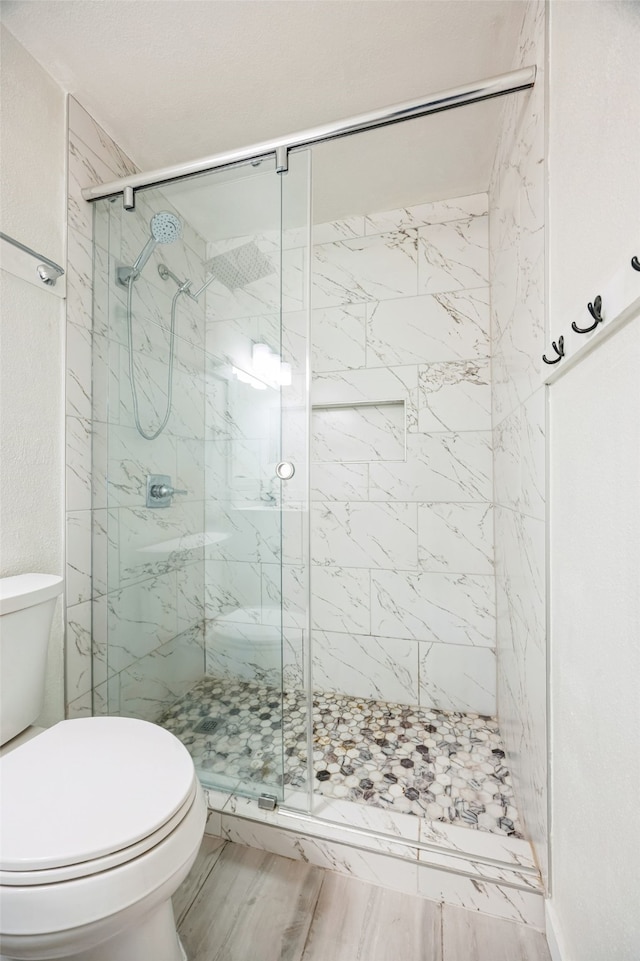 bathroom featuring hardwood / wood-style flooring, a shower with shower door, and toilet