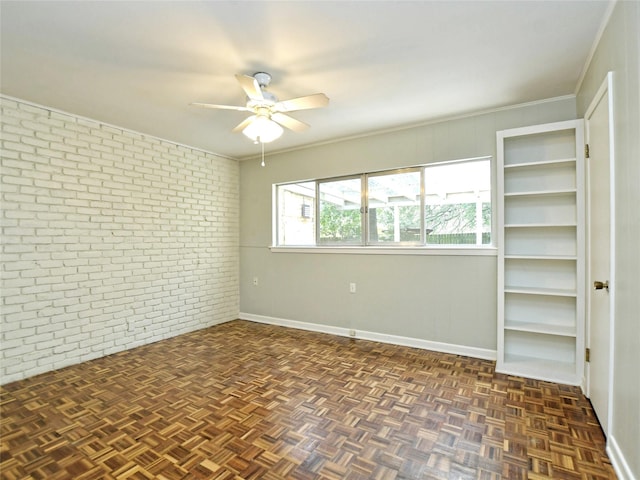 spare room with crown molding, dark parquet floors, ceiling fan, and brick wall